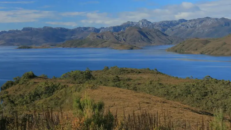 Stunning blue Lake Pedder in Gordon Dam Wilderness, encircled by lush hills and dramatic mountains, Tasmania’s scenic gem.