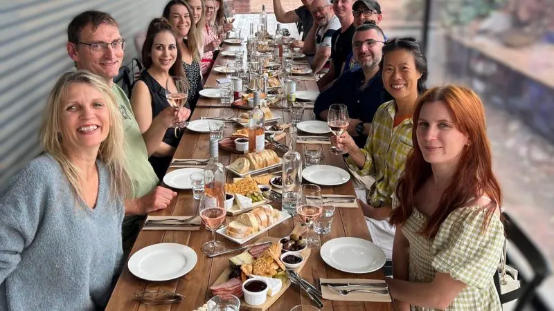 Smiling guests enjoy a premium wine tasting, raising glasses around a rustic table on the Taste The Barossa Premium Wine Tour.