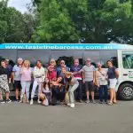 Happy group posing in front of Taste The Barossa Premium Wine Tour coach, parked on a scenic street for a memorable South Australia wine tour.