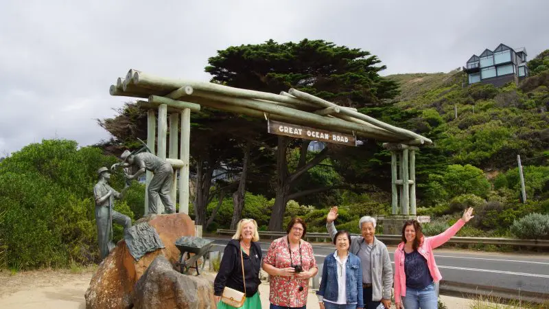 Five women smiling and waving at the iconic Great Ocean Road Memorial Arch during a 4-day, 3-night Great Ocean Road and Beyond tour.