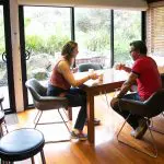 Two travellers sipping coffee by a lush garden view, discussing their Great Ocean Road and Beyond 4 Day 3 Night itinerary in detail.