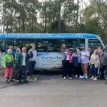 Smiling group poses by a vibrant blue Great Ocean Road And Beyond 4 Day 3 Night Tour coach, ready for an unforgettable adventure.