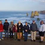 Group of eight on a wooden lookout, stunning ocean cliffs behind, during Great Ocean Road and Beyond 4 Day 3 Night Tour adventure.