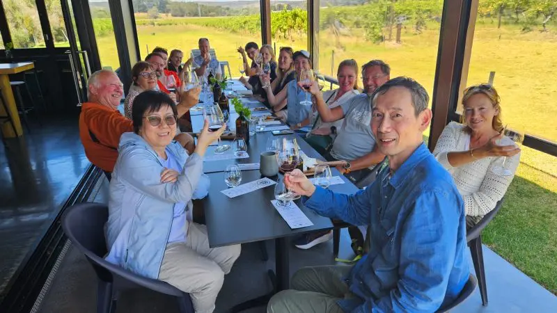 Happy group toasting with wine at a bright outdoor Adelaide restaurant, enjoying the Highlights and Coast Full Day Wine Tasting tour.
