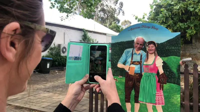 Two people pose with faces in a German-themed cut-out as someone takes their photo during Adelaide wine tasting and coastal tour.