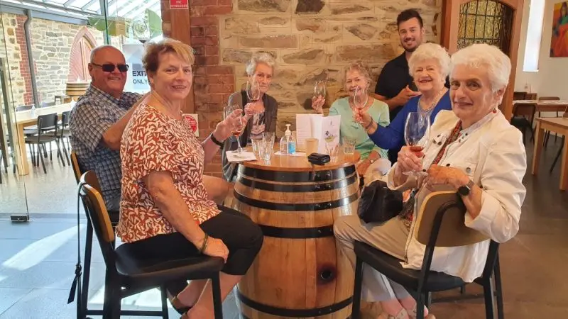 Six pensioners savour premium wine at a rustic barrel table during an immersive full-day Adelaide Highlights tour featuring top tastings.