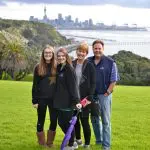 Group of friends smiling on a grassy hill overlooking Auckland skyline and harbour, capturing iconic city highlights and vibrant atmosphere.