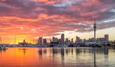 Stunning Auckland City skyline at sunset, boats docked in the harbour, calm waters reflecting vivid colours for a breathtaking view.