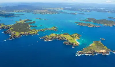 Stunning aerial view of vibrant green islands, boats, and famous Hole in the Rock in New Zealand’s scenic Bay of Islands.