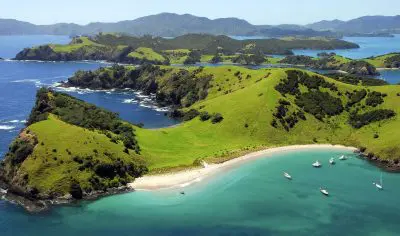 Aerial panorama of New Zealand’s Bay of Islands, featuring pristine sandy beaches, vibrant turquoise waters, and anchored boats.