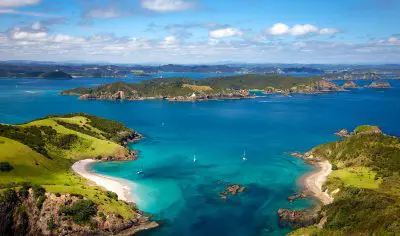 Aerial view of Bay of Islands, showcasing turquoise waters, pristine sandy beaches, lush green islands, and a vibrant blue sky.