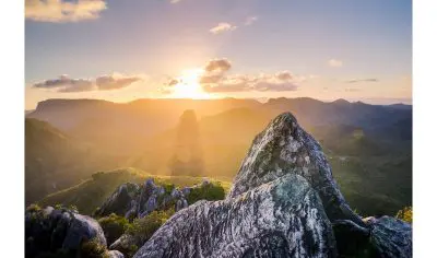 Breathtaking rocky mountain peaks lit by golden sunset, overlooking rolling hills under a dramatic sky, perfect for a forest tour adventure.