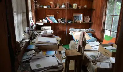 Sunlit wooden room cluttered with books and travel papers, suggesting detailed planning for a scenic Coromandel tour.
