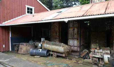 Weathered vintage machinery stands in front of a rustic red wooden building, iconic for Coromandel sightseeing and travel photography.