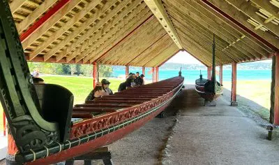 Tourists admire two impressive wooden Viking ships beneath an open waterfront shelter, highlighting Norse maritime history.