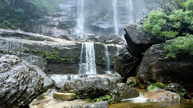 Spectacular tall waterfall pours over rugged cliffs in the Blue Mountains, surrounded by lush greenery on a sunset wilderness day tour.