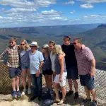 Group of seven enjoying panoramic Blue Mountains lookout on a 1 Day Sunset Wilderness Tour, dramatic clouds overhead, scenic views.