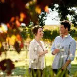 Happy couple savouring white wine amid lush Hunter Valley vineyards on a sunny 1 Day Scenic Wine Tour, perfect for wine lovers.