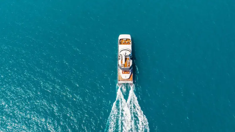 Stunning aerial view of a luxury yacht cruising near Whitehaven Beach, gliding through crystal-clear turquoise waters, leaving white trails.