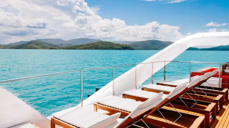 Luxury yacht deck with sun loungers faces crystal-clear turquoise waters at Whitehaven Beach—ultimate all-day relaxation, no snorkelling.