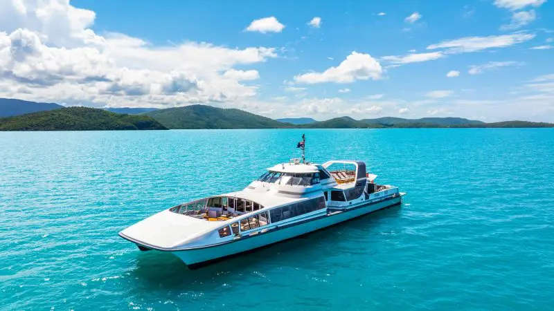 Luxurious white yacht anchored on vibrant turquoise waters near Whitehaven Beach, surrounded by lush green islands, no snorkellers visible.