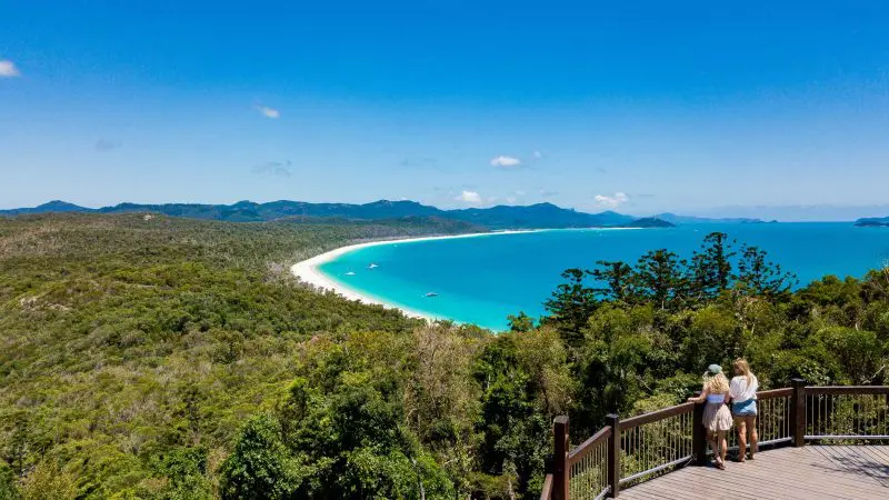 Two people on a wooden lookout gaze over Whitehaven Beach’s pristine white sand and vibrant turquoise sea, enjoying unbeatable scenic views.