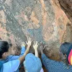 Group of four travellers reach towards ancient rock art on a 7-Day Adelaide to Uluru Adventure with Untamed Escapes, showcasing heritage.