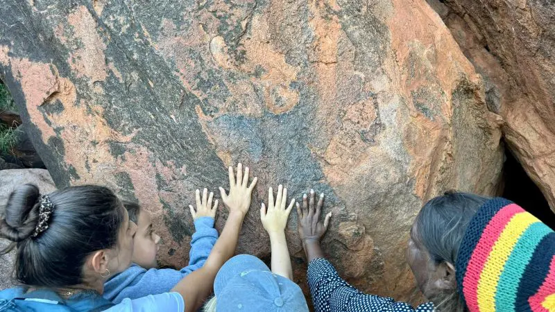 A group of four, guided by an elder in a vibrant hat, explore ancient Aboriginal art on the 7 Day Uluru to Adelaide Untamed Escapes tour.