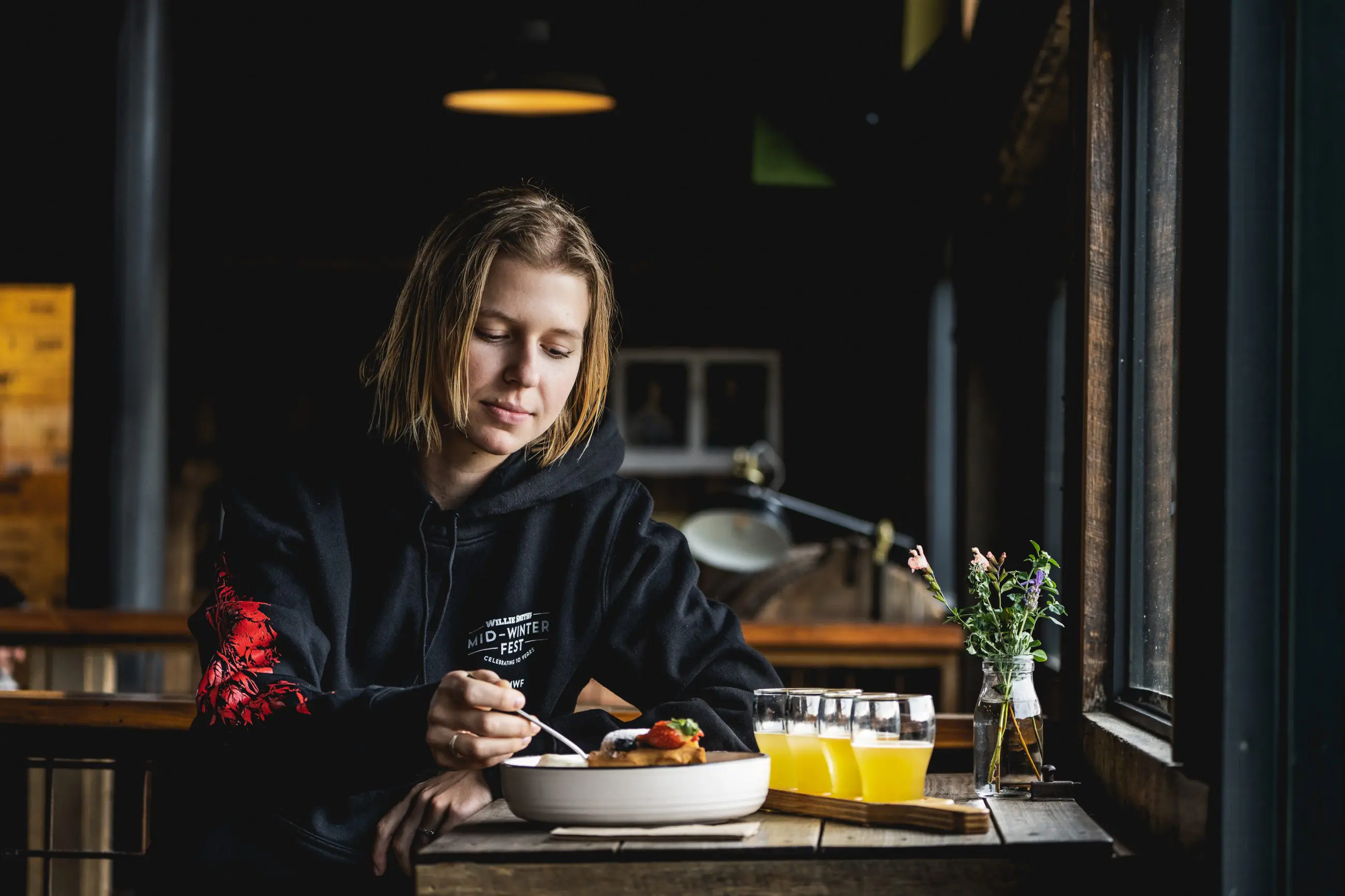 Traveller enjoys fresh meal by a sunny window on Huon Valley Safaris Private Day Tour, with juice and flowers elegantly set on table.