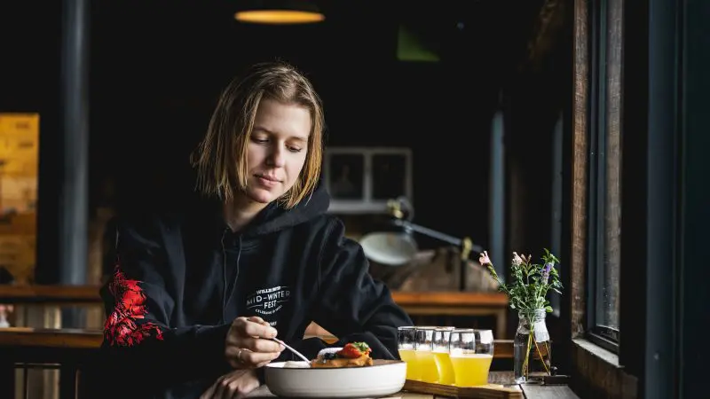 Traveller enjoys fresh meal by a sunny window on Huon Valley Safaris Private Day Tour, with juice and flowers elegantly set on table.