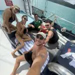 Five friends smile and relax on a boat under sunny skies during their East Coast Explorer tour, capturing a fun group selfie moment.