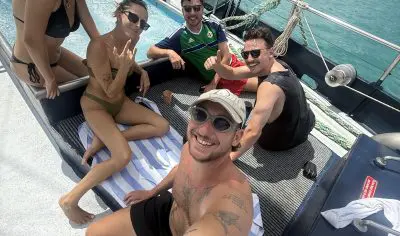 Five friends smile and relax on a boat under sunny skies during their East Coast Explorer tour, capturing a fun group selfie moment.