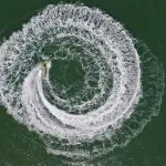 Aerial drone shot of a jet ski carving perfect spiral waves, resembling an Espresso Martini’s swirl in rich white froth.