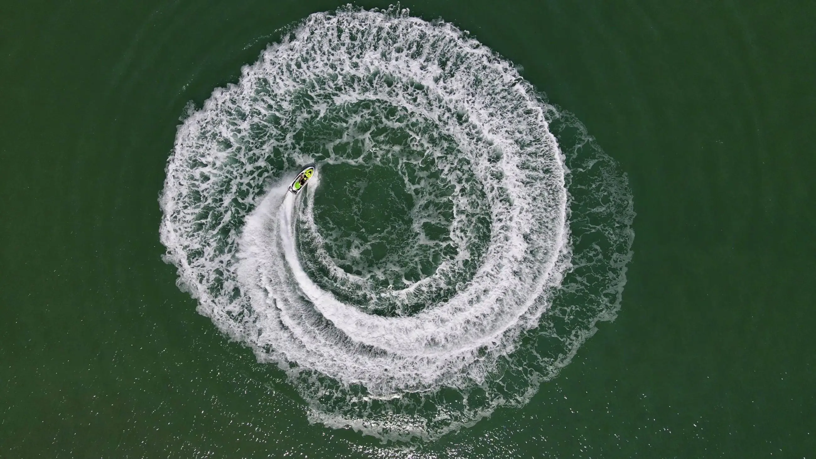 Aerial drone shot of a jet ski carving perfect spiral waves, resembling an Espresso Martini’s swirl in rich white froth.