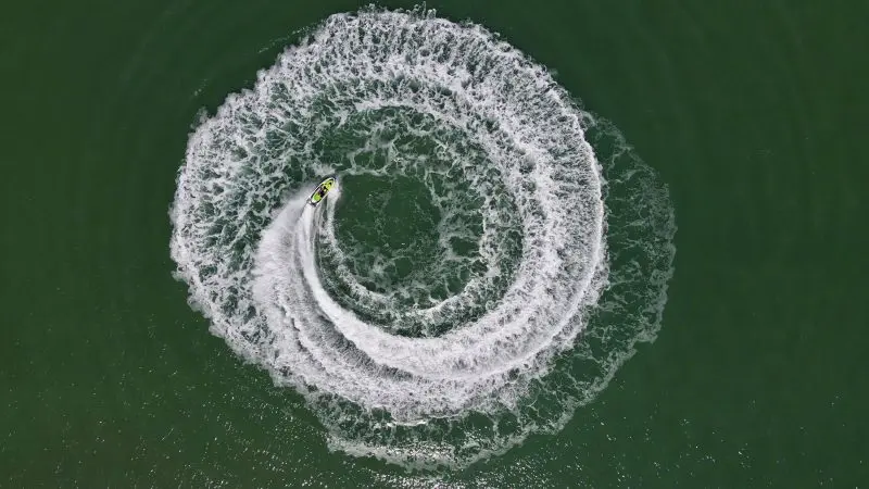 Aerial drone shot of a jet ski carving perfect spiral waves, resembling an Espresso Martini’s swirl in rich white froth.