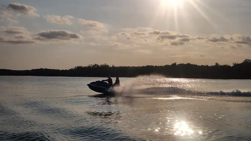 Golden Eye Sunset Tour: two people riding a jet ski on a sunlit lake, water spray sparkling in the golden evening light.