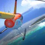 Scenic helicopter soars above vibrant turquoise waters and lush island on a 40 Minute Outer Reef Odyssey under blue sky with clouds.