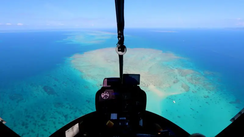 Stunning aerial view from Inner Reef Explorer helicopter touring vibrant blue ocean and coral reefs beneath a crystal clear sky.