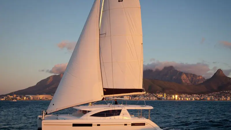 Whitehaven Dreamer catamaran sails at sunset on Whitsunday waters, cruising past scenic mountains and the vibrant city skyline.
