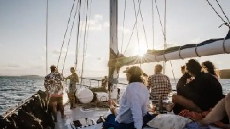 a group of people on the bow of summer jo at sunset