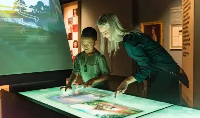 A woman and boy interact with a large interactive touchscreen exhibit at New Zealand’s Waitangi Treaty Grounds museum display.