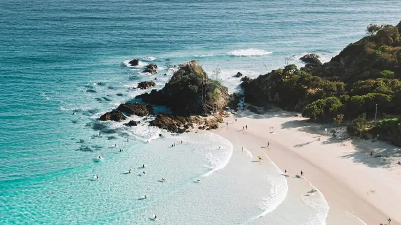 Stunning aerial shot of a sunlit sandy beach with surfers riding waves, ideal for The Great Escape Australia 28 Day Semi-Guided adventure.