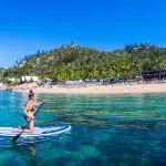Woman kayaking on crystal-clear blue water beside lush palm trees, evoking The Great Escape 21-Day Trip from Brisbane to Cairns.