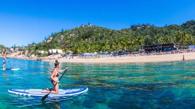 A woman kneels on a paddleboard in crystal-clear blue water during The Great Escape Australia 28 Day Semi-Guided adventure tour.