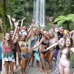 Energetic young travellers in swimwear smile and pose by a stunning waterfall on The Great Escape Australia 28 Day Semi-Guided tour.
