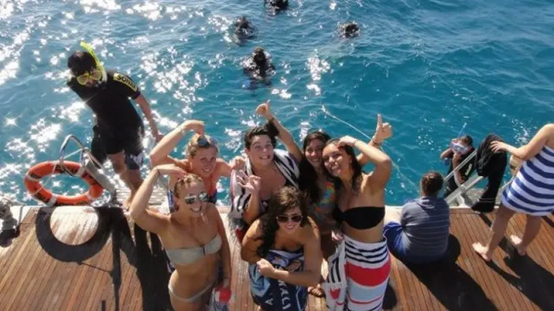 Smiling friends in swimwear enjoy a sun-filled boat ride on The Great Escape Australia 28 Day Semi-Guided tour adventure.