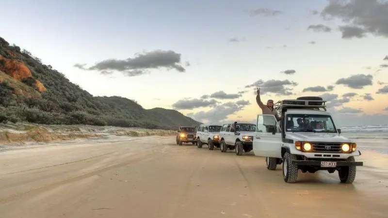 Off-road vehicles from The Great Escape Australia 28 Day Semi-Guided Tour traverse a scenic sandy beach adventure route.