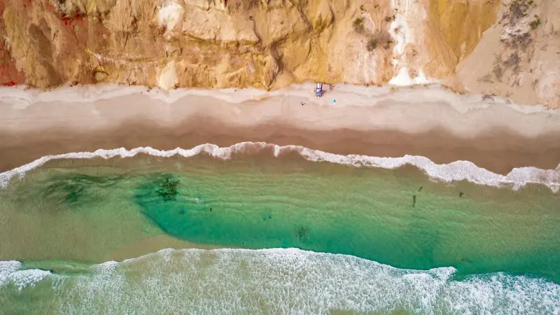 Aerial view of vibrant turquoise ocean waves crashing against golden cliffs on The Great Escape Australia 28 Day Semi-Guided adventure tour.