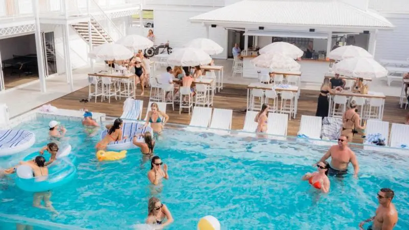 People swim and play with beach balls at a lively, sunny Australia group trip resort with white buildings.