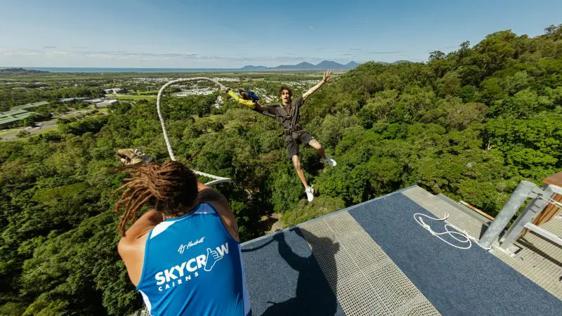 Thrilling bungee jump at Roof Jump Skypark: adventurer leaps from platform above lush forest, guided by instructor, mountains scenic backdrop.